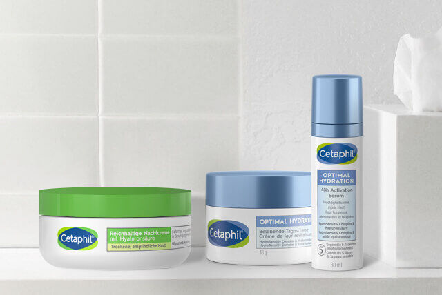 Drei Cetaphil Gesichtspflege-Feuchtigkeitscremes für empfindliche Haut auf einem Badezimmerregal vor weißen Badezimmerfliesen. 