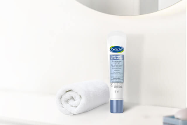 Cetaphil Produkte für die Pflege der Augenpartie auf einem weißen Badezimmer Sideboard mit Handung und vor weißer Wand mit Spiegel